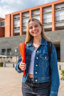 Happy young blonde woman with a backpack and a red folder, smiling confidently while standing