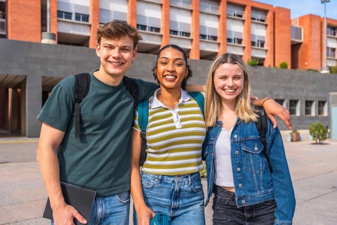 Three young multiethnic students with backpacks posing and smiling at the camera, standing in front