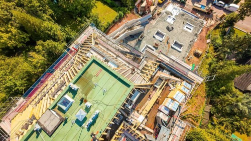 Aerial view of a construction site with roof structures and materials in a green environment,