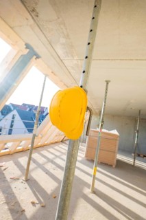 A yellow safety helmet hangs on a metal support on a construction site in sunlight, carpentry