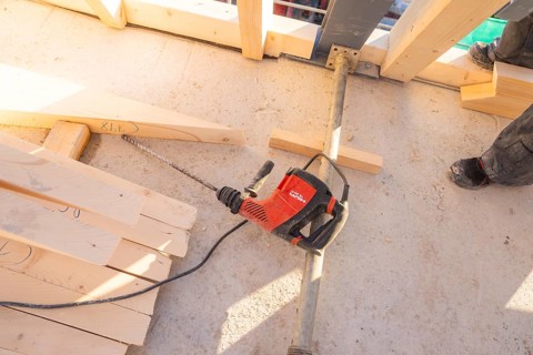 A drill is lying on a construction site floor, surrounded by wooden planks and a pair of shoes,