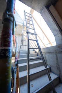 A steel staircase leads to a ladder under a concrete opening that leads upwards, carpentry