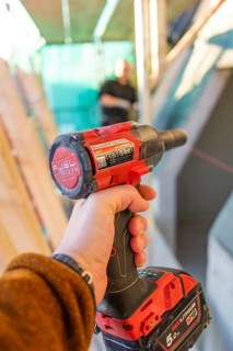A worker holds a red electric screwdriver in a construction site situation, carpentry construction,
