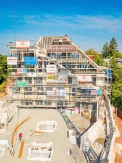 Construction site of a large building with several floors, surrounded by trees and scaffolding,