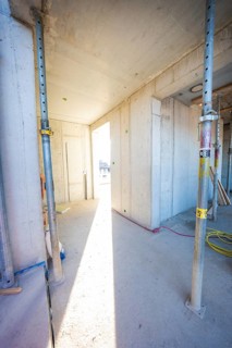 A sunlit corridor in an unfinished building with concrete walls and metal supports, carpentry