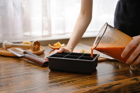 A person is pouring a blend of sea buckthorn, orange and ginger into a silicone ice tray on a