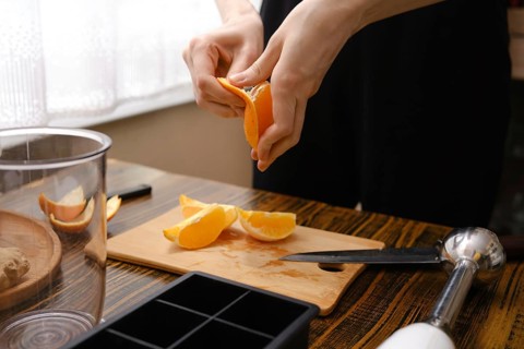 A person peels orange slices on a wooden cutting board in the kitchen during the process of