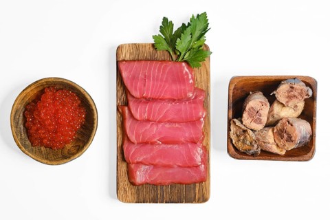 Sliced cured tuna fillets and canned tuna are on a wooden board, accompanied by a bowl of red fish