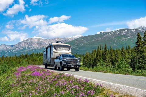 Off-road vehicle with caravan on highway, road through taiga and mountain landscape with purple