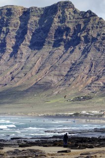 Beach with rocks and cliffs (Risco de Famara) in the background, people enjoying the sea, Caleta de