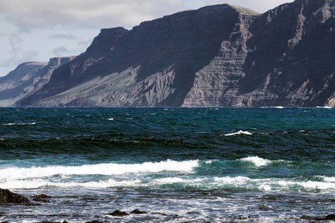 Coast with thundering waves and high mountains in the background Risco de Famara) under partly