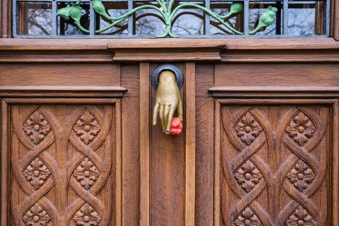 A cast iron door knocker on a wooden, artfully decorated front door in the shape of a hand holding