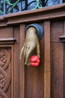 A cast iron door knocker on a wooden, artfully decorated front door in the shape of a hand holding