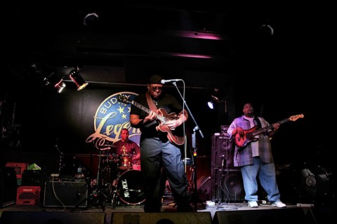 Blues musicians perform vividly on a club stage, accompanied by intensive guitar and drum music,