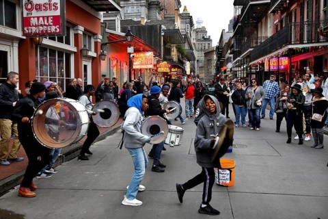 Musicians play on bustling Bourbon Street in the French Quarter. Drums and people create a lively