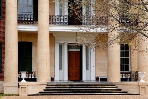 Entrance of an elegant house with large pillars and wooden door, surrounded by trees, Natchez,
