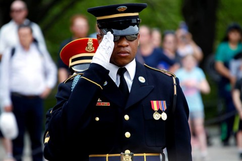 Soldier in uniform salutes during a solemn ceremony, spectator in the background, Washington D.C,