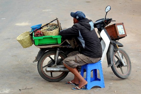 Dealer pauses on a blue stool next to his motorbike loaded with baskets, Oulidia, Doukkala-Abda,
