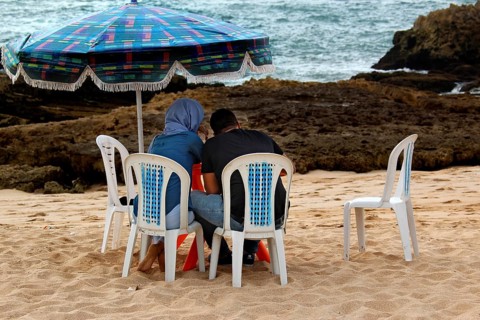 Two people sitting under a colorful sunshade on the beach in Oulidia, Oulidia, Morocco