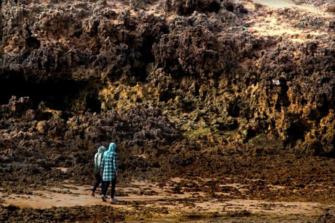 Person walking along rocky stretches of beach in Oulidia, Morocco, Oulidia, Doukkala-Abda, Morocco