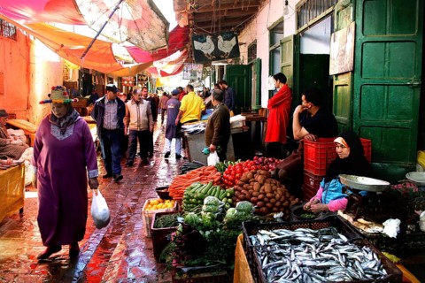A lively market scene with a variety of fresh vegetables and people passing by, Tetouan, Medina,