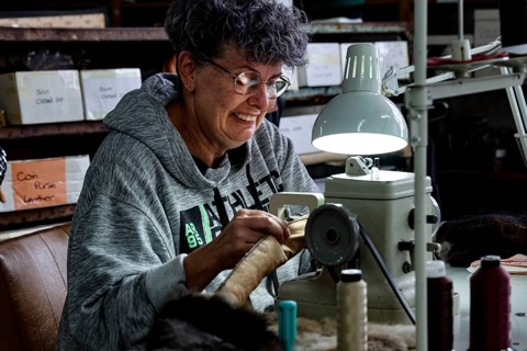 Seamstress works concentrated with thread and material under a lamp in a Possum factory, Stratford,