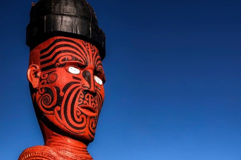 Large carved Maori figure painted red against deep blue sky in Whakarewarewa village, Rotorua,