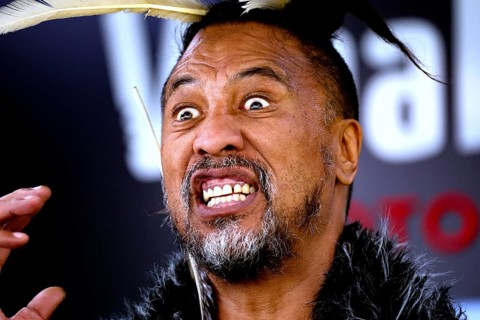 Maori man with aggressive facial expressions and feather headdress at a performance, Rotorua, Bay