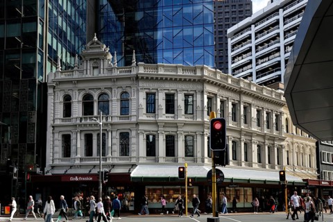Busy intersection with historic façade contrasting with modern glass buildings on Lambton Quay,