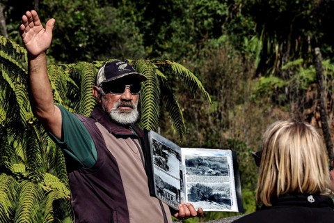 Tour guide points to surroundings surrounded by nature and holds a book, Whanganui River, New