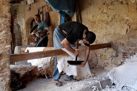 A man works on leather goods in an old workshop with rustic charm, Fez, Fez el Bali, Morocco