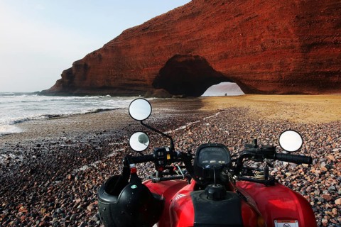 Quad bike on beach with impressive rock arch in Legzira, Legzira, Morocco