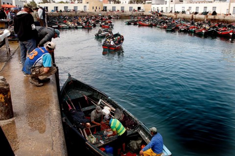 Boats in the calm waters of the harbor with fishermen working on the quay wall, El Jadida, harbor,