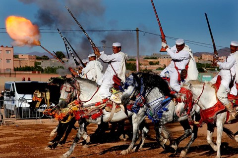 Riding group shoots in sync with rifles and creates fire and smoke in the midst of a traditional
