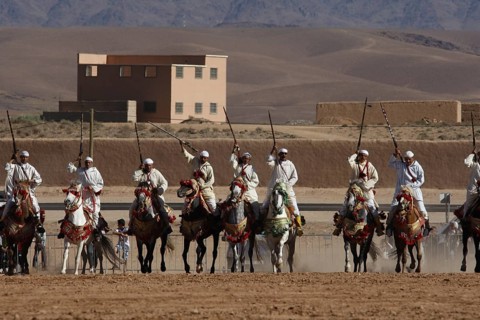 Riders in formation on a wide terrain with mountain scenery during Fantasia, El Kelâa m'Gouna,