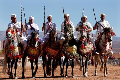 Six riders side by side on decorated horses at Fantasia, El Kelâa m'Gouna, Morocco