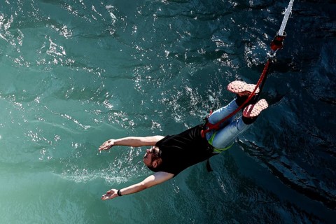 Person bungee jumping with arms extended over water, Queenstown, Kawarau Bridge, New Zealand