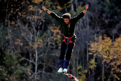 Person with arms spread out bungee jumping in front of autumn landscape, Queenstown, Otago, New
