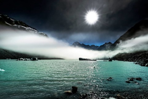 Turquoise glacial lake under bright sun and mystical fog