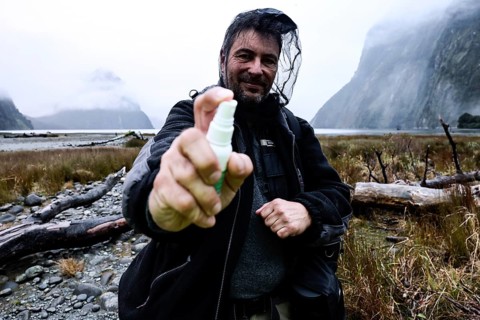 Man wearing outdoor clothes with mosquito repellent and head net in foggy mountain backdrop,