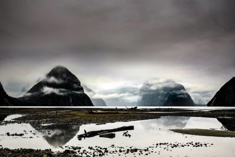 Mirroring water surfaces and mist-covered mountains in Milford Sound create a calm, mystical