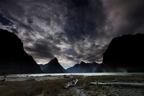 Dramatic clouds in the sky over Milford Sound at dusk, framed by silhouettes of mountains, zero