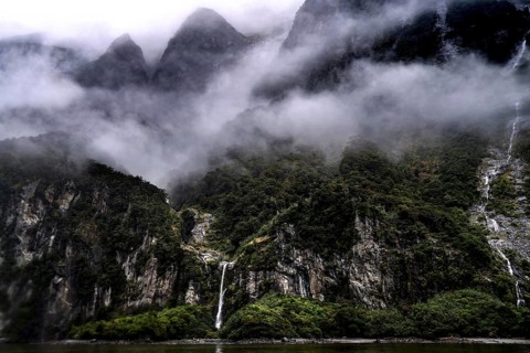 Foggy mountains and steep slopes in Milford Sound, surrounded by clouds and green vegetation, zero
