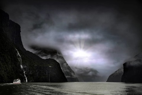 Fjord landscape with a cruise ship, sun rays breaking through the cloud cover, Milford Sound, New