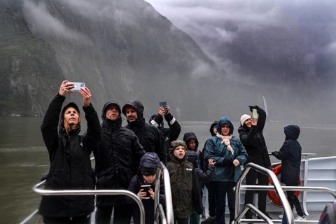 Group of passengers take pictures of the misty landscape from a cruise ship, Milford Sound, New