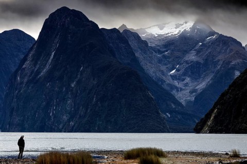 Lonely hiker on the banks of Milford Sound, with snow-capped mountains in the background, zero