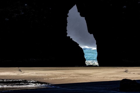 View through a crevice of the glowing sea at Piha Beach, Piha Beach, region, New Zealand
