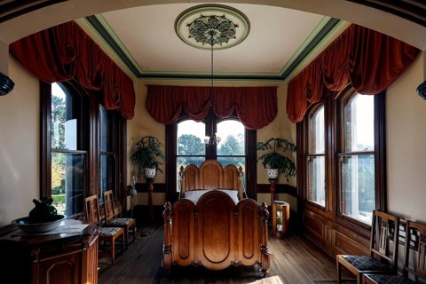 Comfortable bedroom with fine furnishings, large windows and red curtains, Larnach Castle, Otago