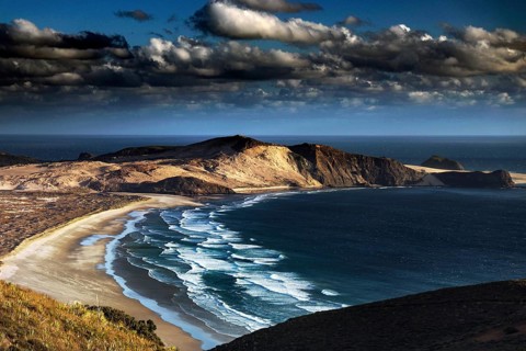 Dramatic coastal landscape with sweeping beaches and wild waves under a cloudy sky, Cape Reinga,
