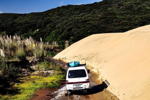 Off-road vehicle drives through sandy dunes along a small river